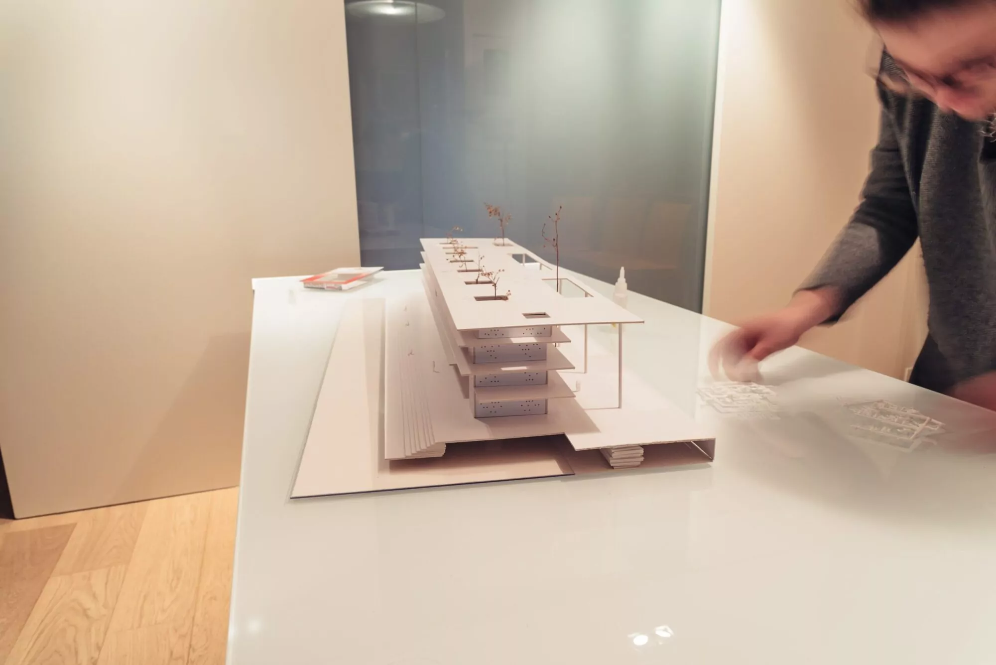 A designer assembling a scale model of a modular trade show booth with layered structures and intricate details.