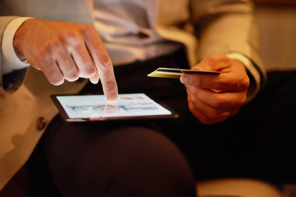 Person using a tablet and holding a credit card, symbolizing digital transactions and investment in launching online scratch card platforms.