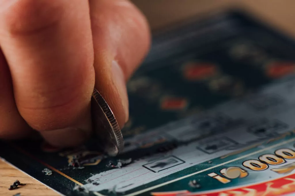 close up view of silver coin in hand of gambler scratching lottery ticket
