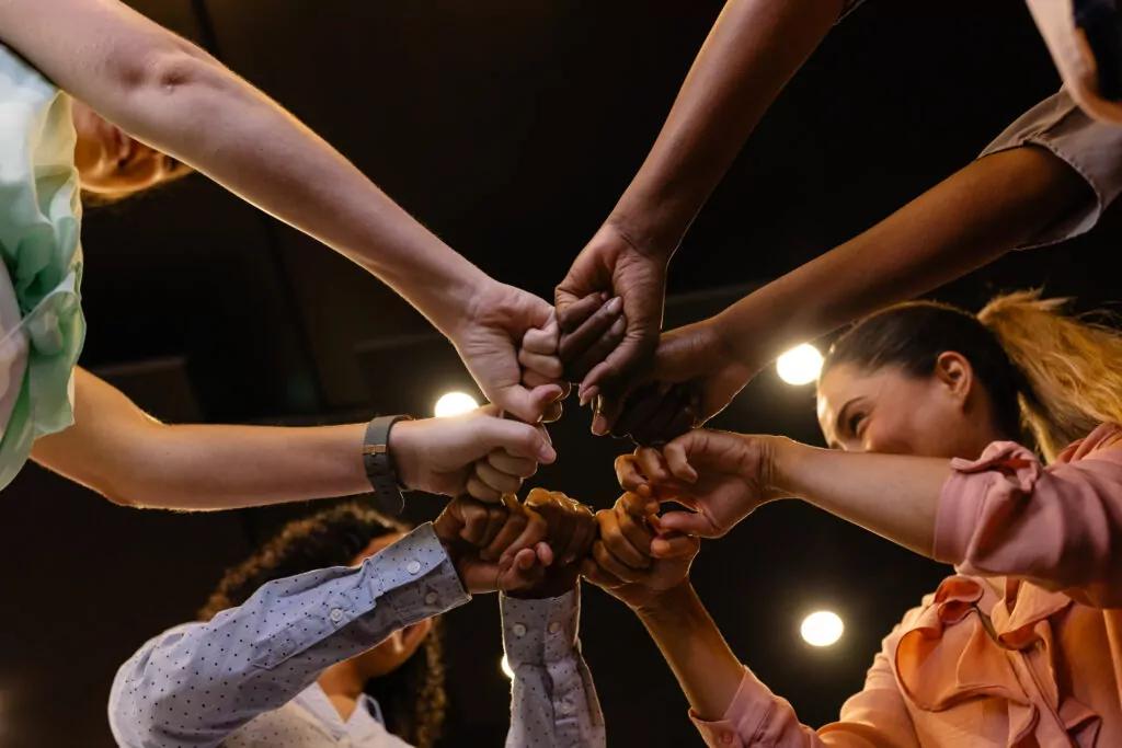 Happy diverse casual businesswomen holding hands in office. Casual office, business, teamwork and work, unaltered.