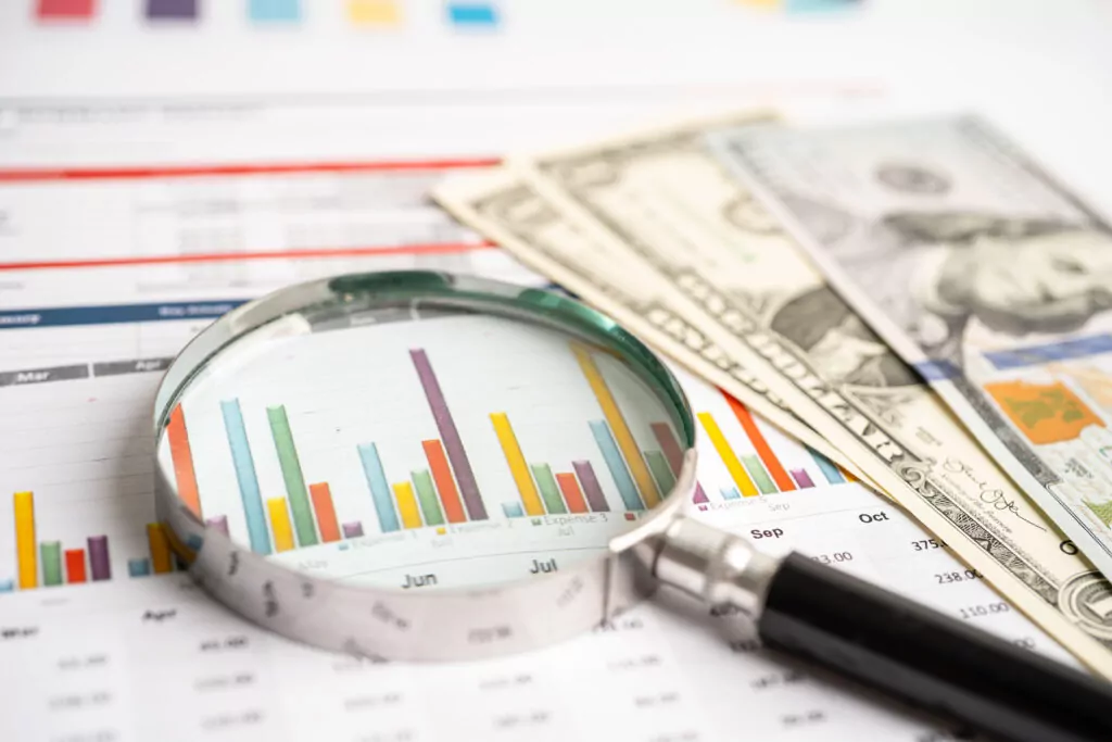 Magnifying glass on data charts graphs paper with US dollar banknotes