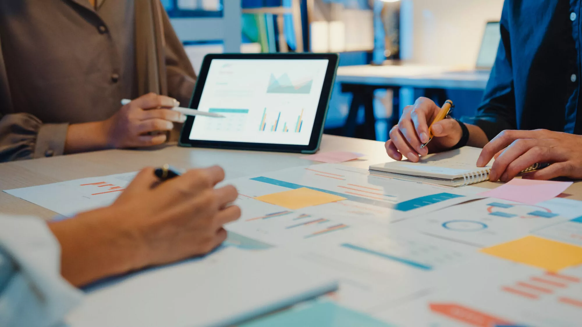 Data analysts reviewing charts and customer data on a tablet and paper for in-store kiosk marketing strategies.